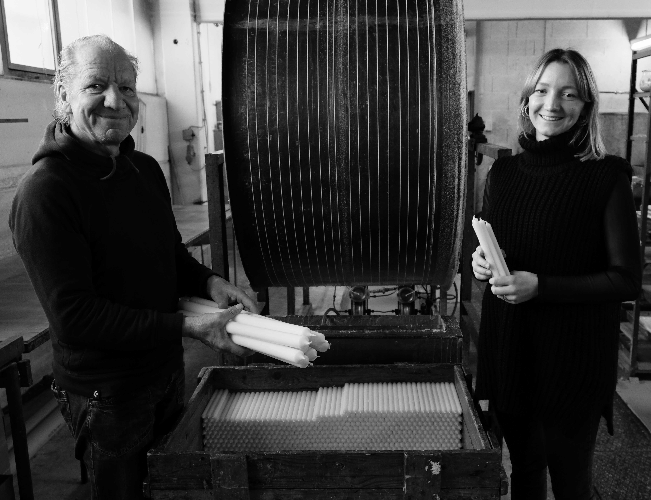 Schwarz Weiss Foto von Joerg und Pia Zengerle in der Werkstatt vor der Zugmaschine neben einer mit Kerzen befüllten Holzkiste; beide haben Kerzen in der Hand